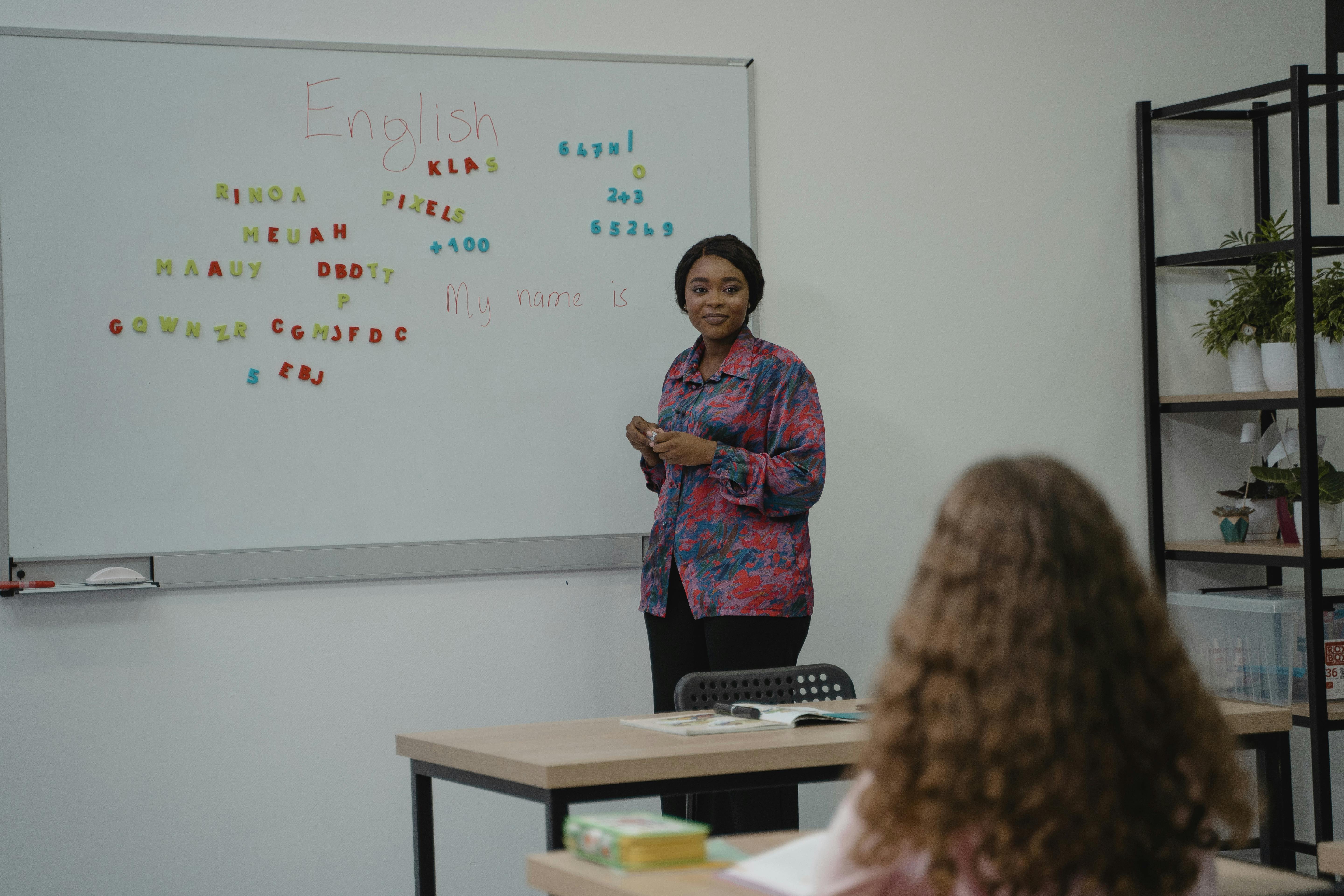 Home A teacher explaining English concepts to a student in a classroom setting with a whiteboard.